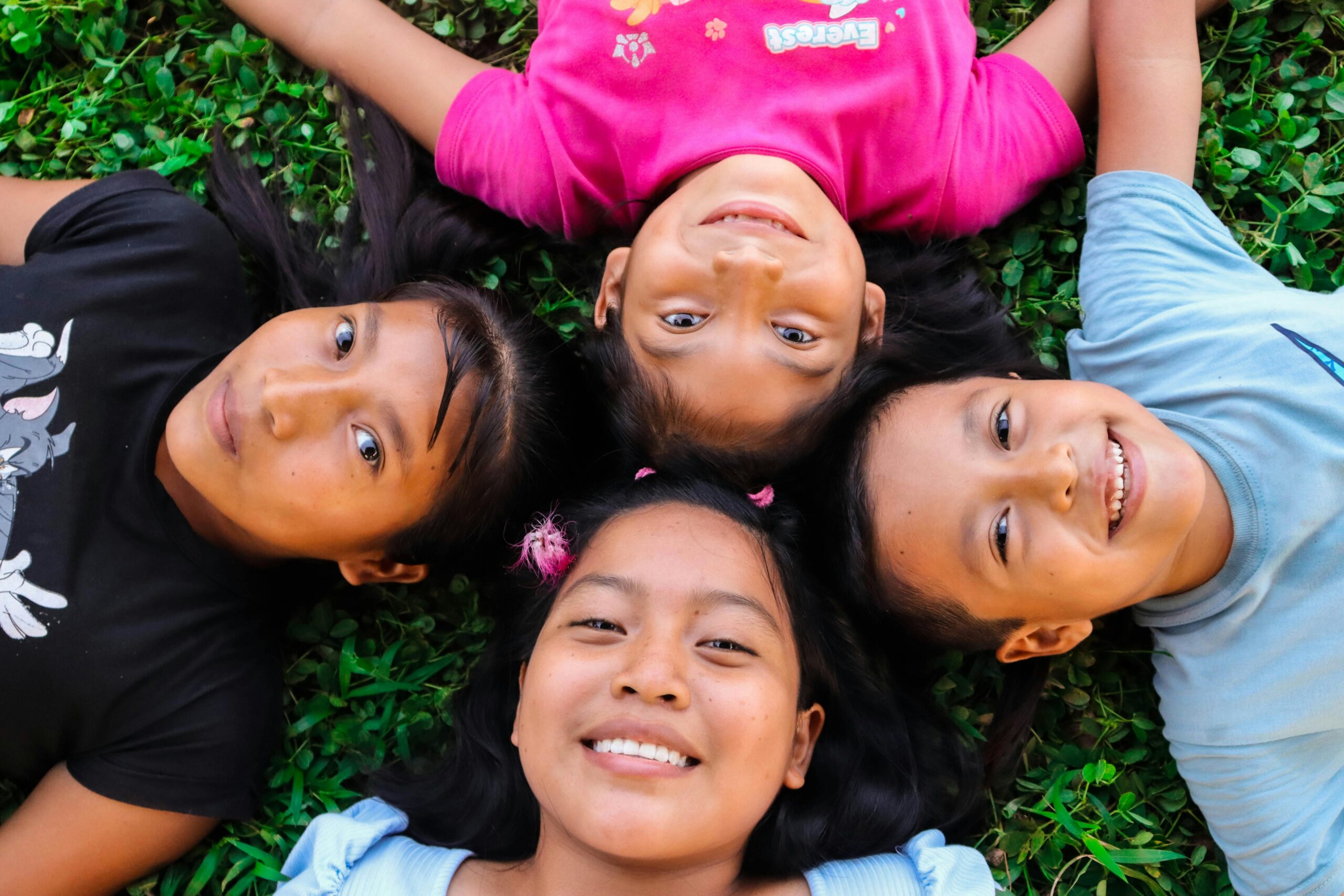 Joyful group of diverse children lying on green grass enjoying a sunny day.